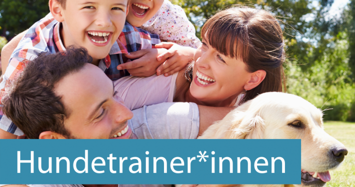 Eine lachende Familie aus Mutter, Vater und zwei Kindern liegt auf dem Gras, sie kuscheln einen Hund und sehen glücklich aus.