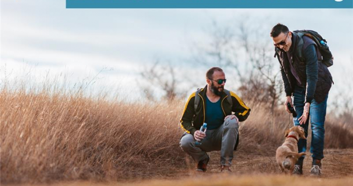 Zwei Männer beschäftigen sich auf einem Feld an einem sonnigen Tag mit ihrem Hund. Über dem Bild steht: Neue Podcastfolge: LGBTQIA+ und Hundetraining