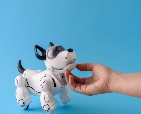Eine menschliche Hand streichelt einen kleinen schwarz weißen Roboterhund, der an einen Terrier erinnert.