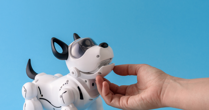 Eine menschliche Hand streichelt einen kleinen schwarz weißen Roboterhund, der an einen Terrier erinnert.
